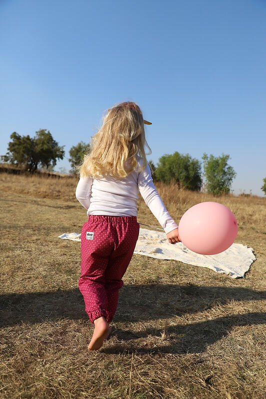 une petite fille dans un champs en pantalion imprimé shweshwe rose avec un ballon rose dans le mains