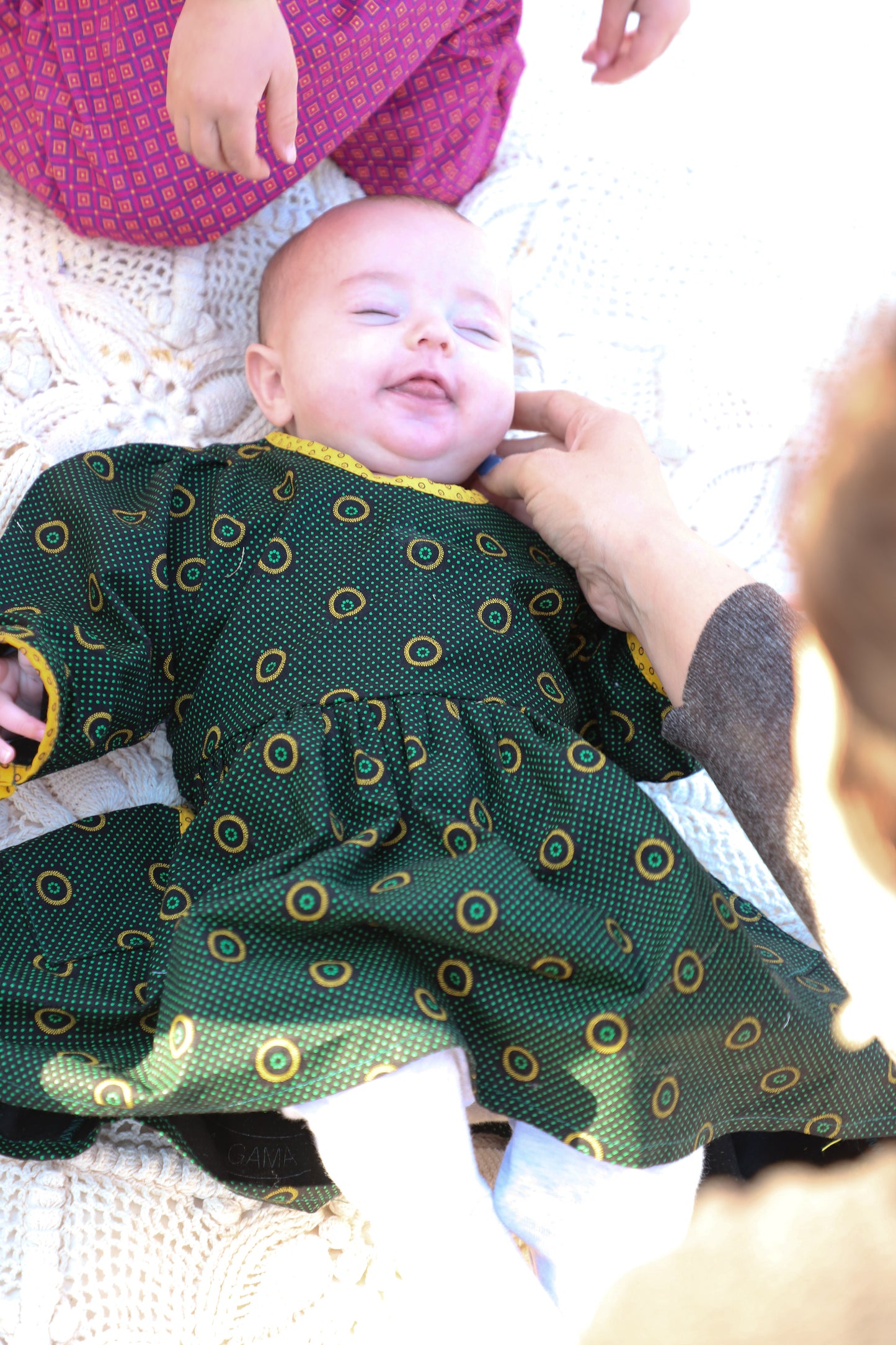 Un bébé fille sur une couverture avec une robe à manches longues imprimé shweshwe vert