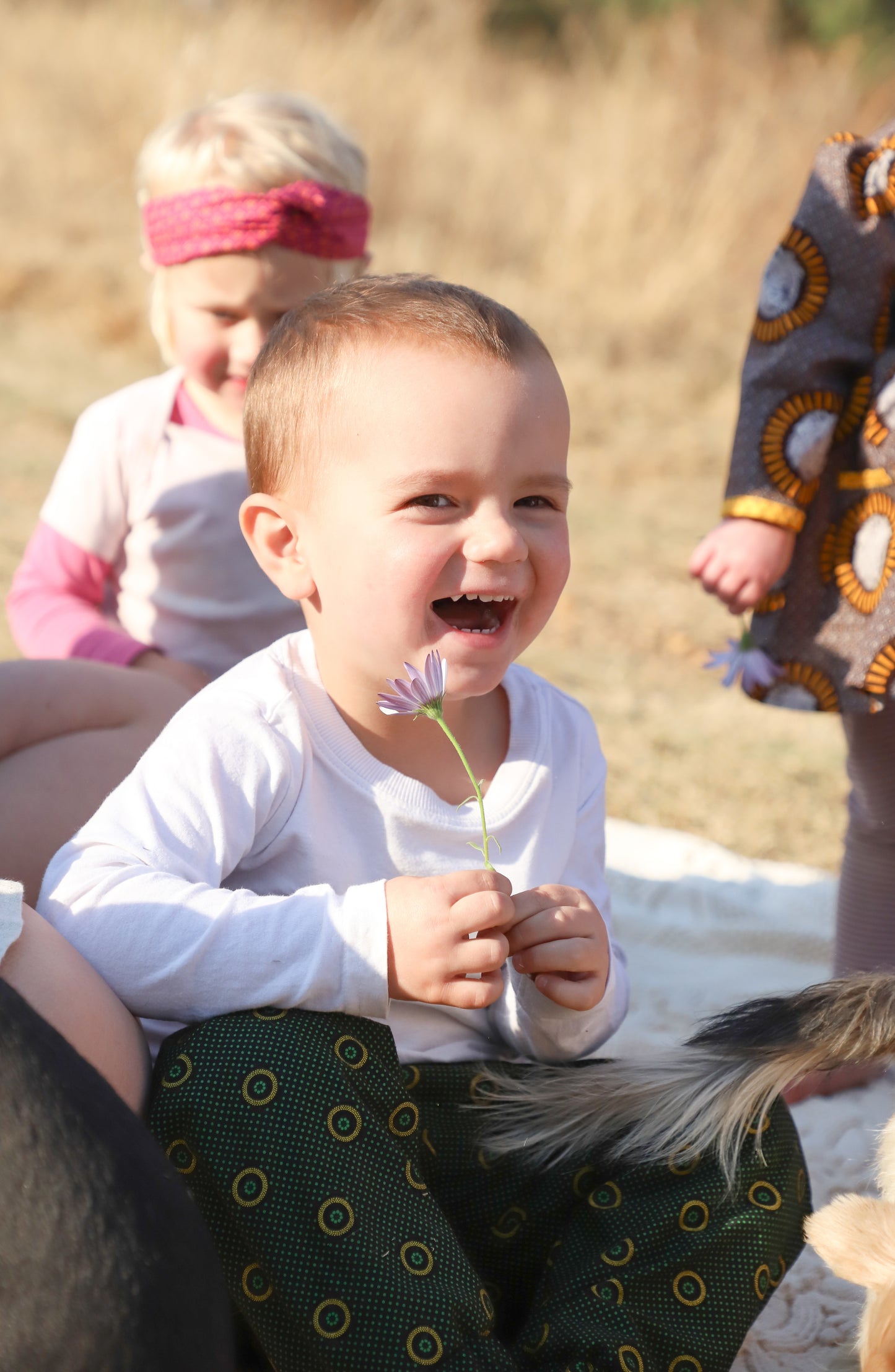 un petit garçon assis sur une couverture avec un pantalon imprimé shweshwe vert avec une fleur dans les mains
