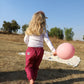 une petite fille dans un champs en pantalion imprimé shweshwe rose avec un ballon rose dans le mains  