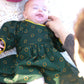 Un bébé fille sur une couverture avec une robe à manches longues imprimé shweshwe vert 